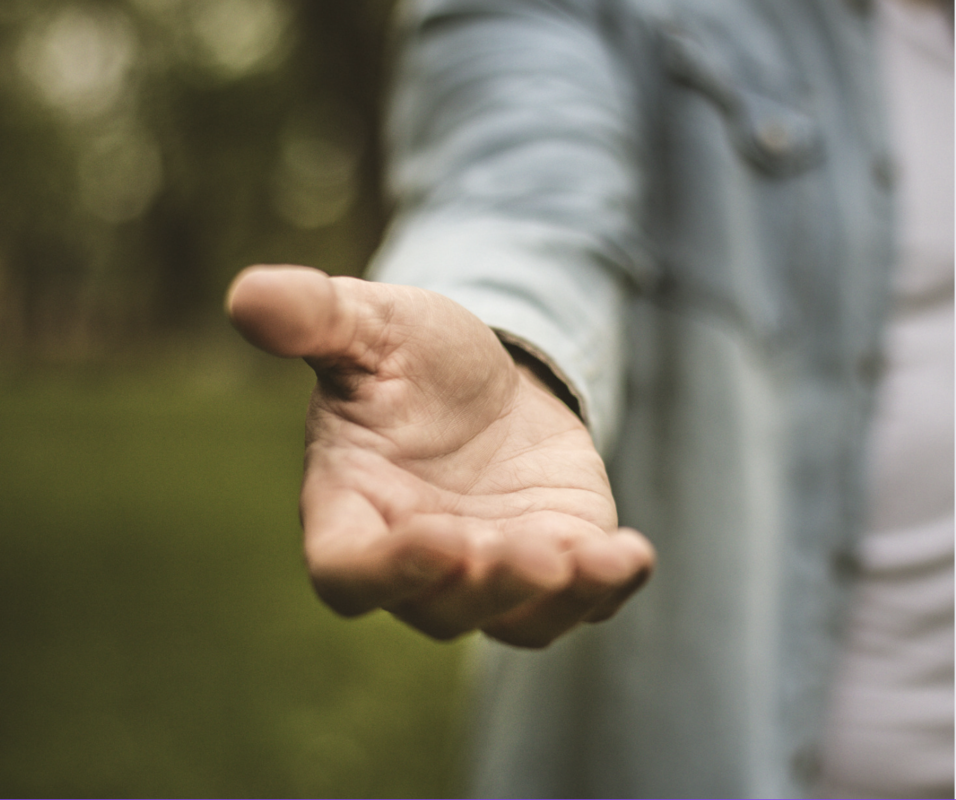 a person holding out their hand in front of a greenery background
